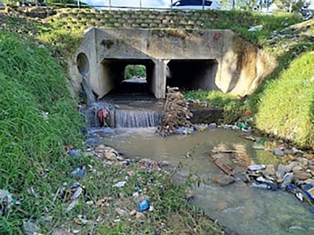 A heavily polluted river runs between high banks under a bridge.