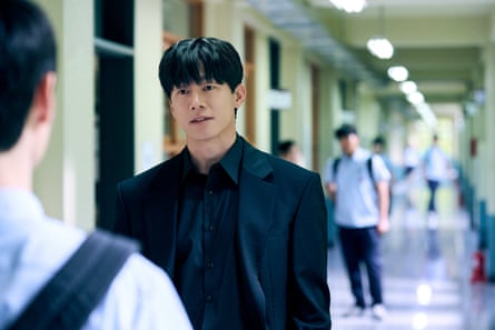 A man in a dark suit in a school corridor