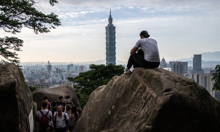 A man sits on a rock overlooking the Taipei 101 tower.
