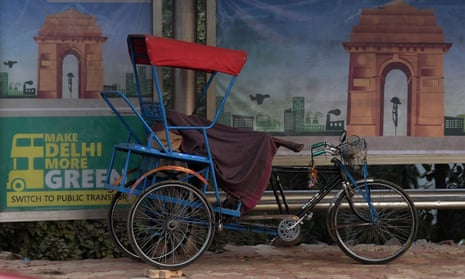 An Indian rickshaw cyclist sleeps next to an advertisement for a more environmentally friendly city, urging residents to switch to public transport, on a foggy morning in New Delhi