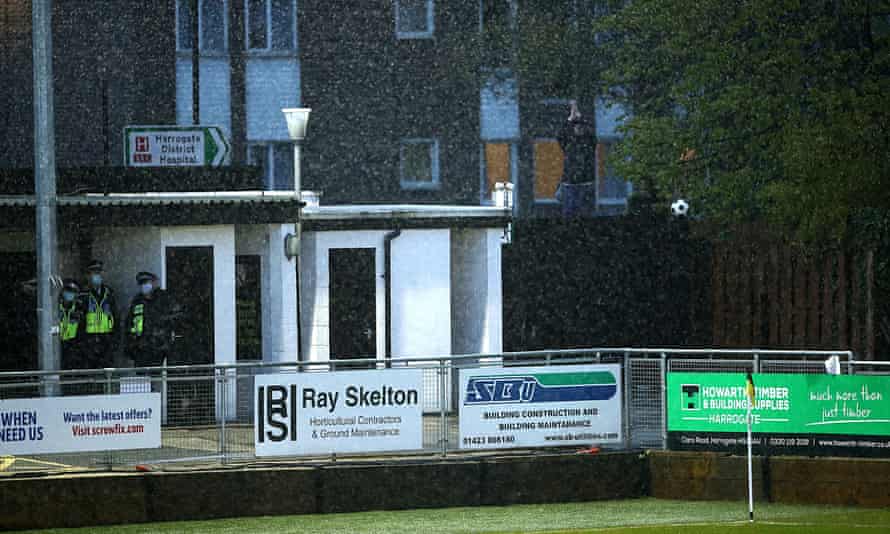 A Cambridge fan stands on a fence to cheer on his side from outside the ground at Harrogate.