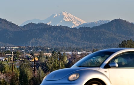 snow-capped mountains above forest hills with silver car in front