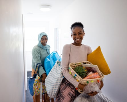 A mother and daughter carry household items down a hallway.