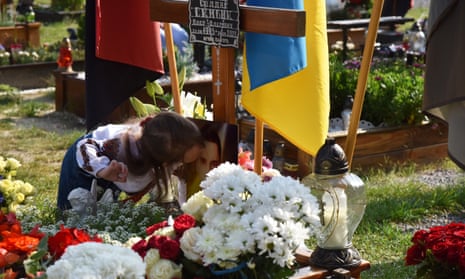 A young girl kisses a photograph of a Ukrainian soldier at a grave covered in flowers