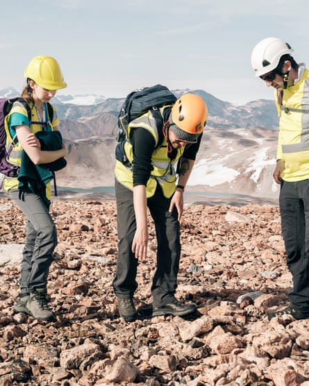 Three geologists examine stones on a rocky plateau.
