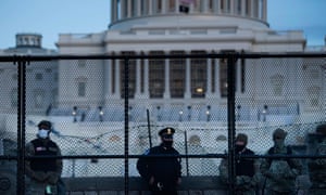 A Capitol police officer stands with members of the National Guard behind a crowd control fence surrounding Capitol Hill on Thursday in Washington DC.
