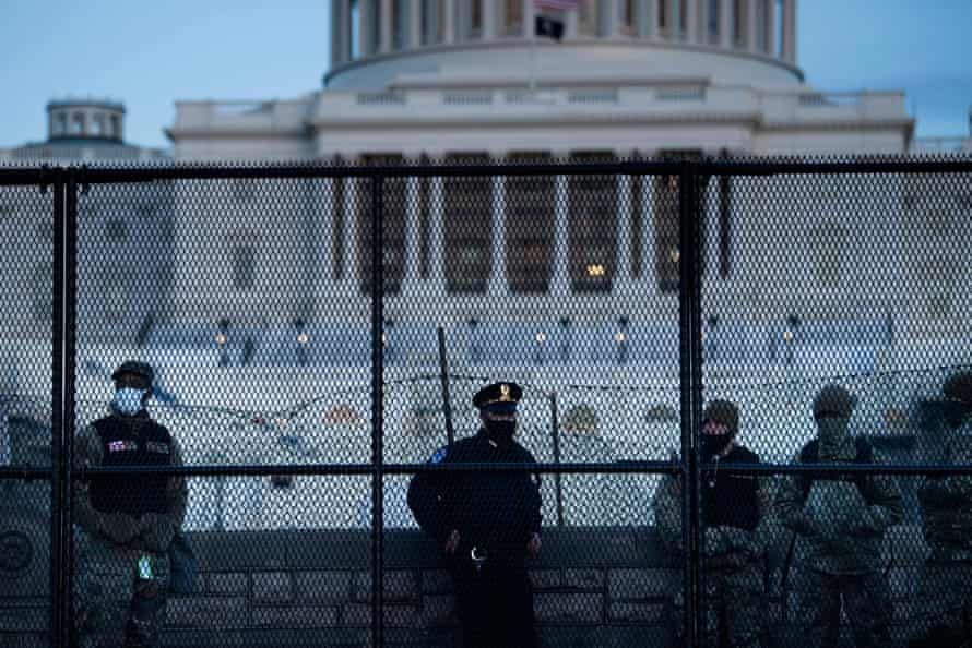A Capitol police officer and members of the national guard stand near a fence surrounding the Capitol.