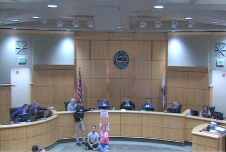 a woman and man sitting in front of a government board