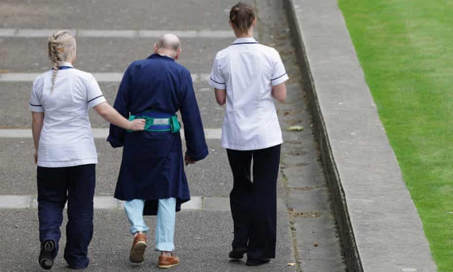 Two NHS staff walk with an elderly patient outside St Thomas’ Hospital in London