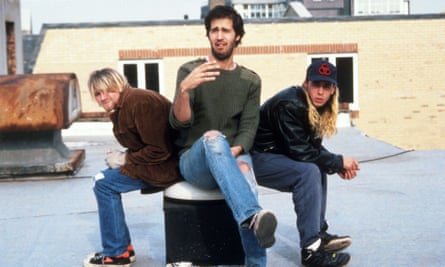Three men of the rock band Nirvana sitting next to each on a round sitting couch.