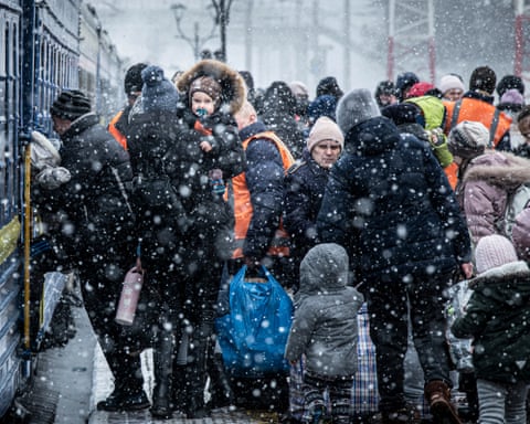 A crowd of people in winter coats and hats stand in heavy snow near a train