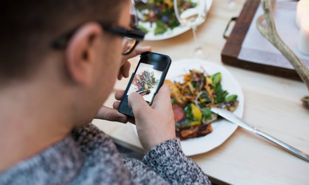 A man photographing a plate of food in a restaurant