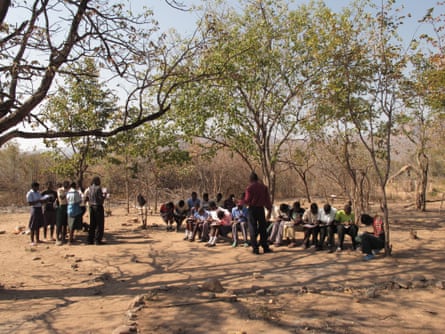 A group of African schoolchildren in an arid savanna landscape writing in notebooks
