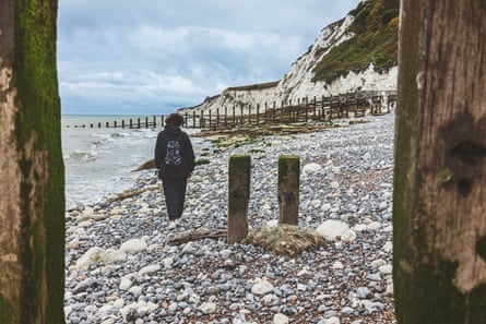A woman walks away from the camera along a pebbled beach