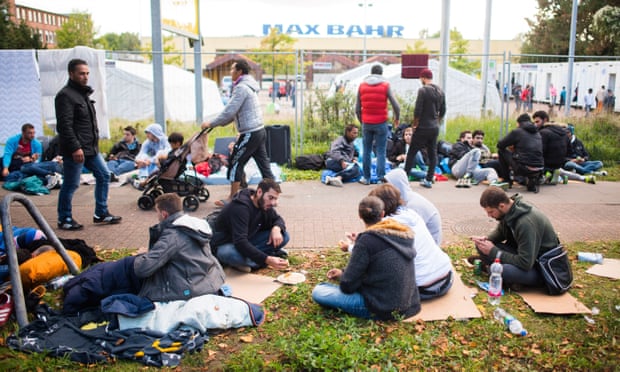 Refugees sit on the grass in front of a refugee shelter in Hamburg