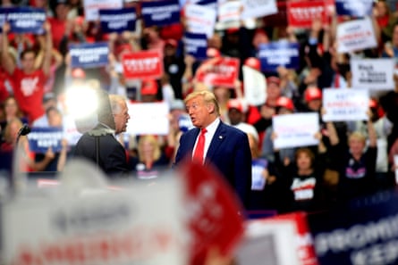 Two men in suits onstage amid a sea of supporters holding red and white signs.