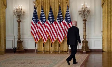 A view of President Joe Biden's back as he walks away. against a backdrop of US flags