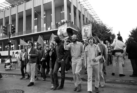 people march with flags and posters of ho chi minh outside a campus building, in a black and white photo