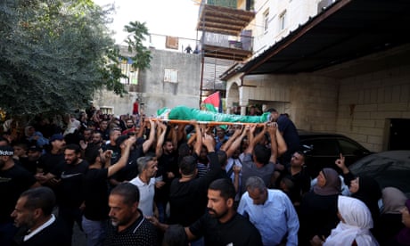 A crowd of people carrying aloft a body covered in a Palestinian flag