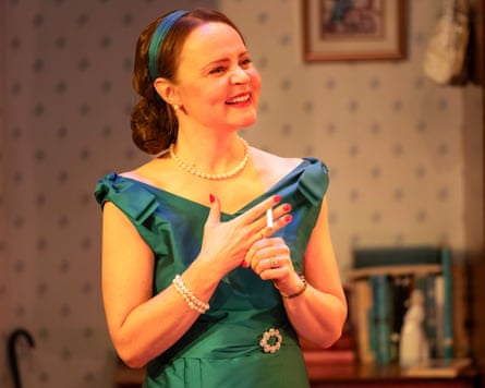 A woman is shown smiling in a green cocktail dress and holding a cigarette in her hand.