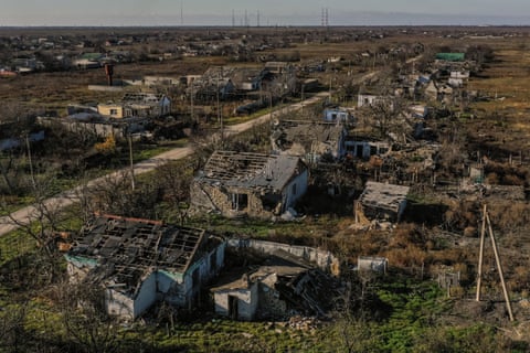 Aerial view of houses with shattered roofs, running along a single-track road in a semi-rural area