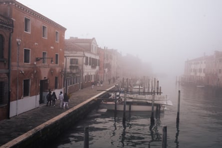 People walk through bankside mist towards moored gondolas