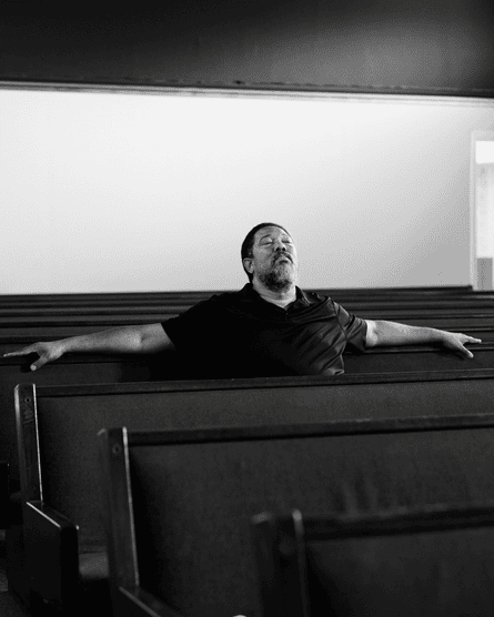 Man sitting on a pew in a funeral home with his eyes shut