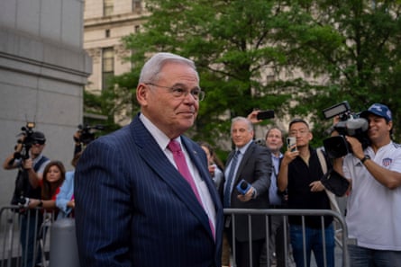 An older man in suit and tie walks past a press scrum.