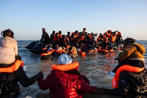 People in orange lifejackets wade out towards an already overcrowded dingy
