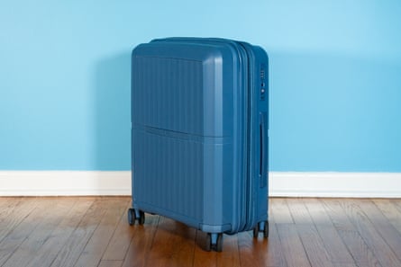 A blue suitcase with wheels on wooden floor in front of blue wall