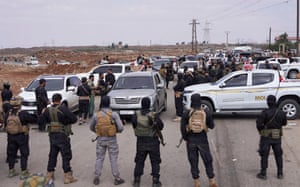 Group of men in the foreground and row of vehicles in front of them