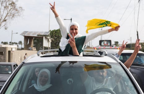 A girl stood out of the sunroof of a car as she shows a victory sign and carries a Hezbollah flag.
