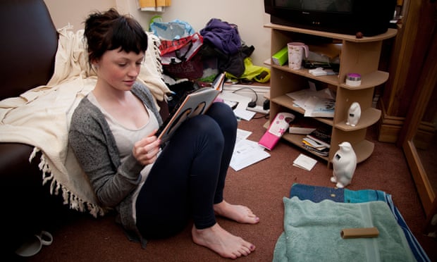 A young woman UK university student reading a book in the living room of her house flat bedsitC2M2G1 A young woman UK university student reading a book in the living room of her house flat bedsit