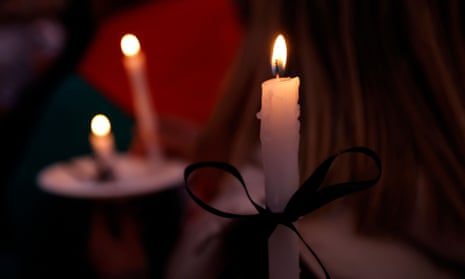 A close-up of white vigil candles tied with black ribbon, with white paper disks at the ends, in the darkness.