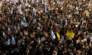 Overhead view of a dense crowd of demonstrators. Some people hold Israeli flags. One placard reads: Bring them home!