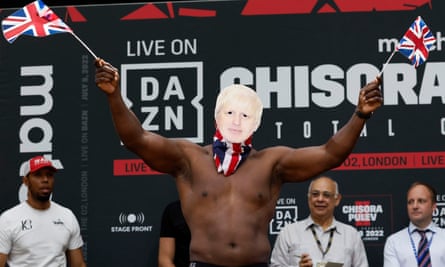 Derek Chisora wears a Boris Johnson mask at a weigh-in for his fight in July 2022.