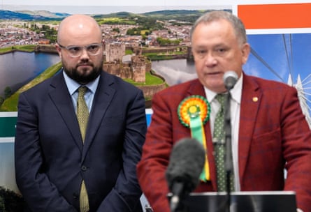 Midshot of Powell listening and Whittle with rosette behind microphone