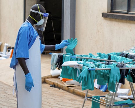 A healthcare worker in protective equipment inspects turquoise gloves hanging on a drying rack