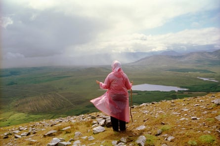 a woman in a pink rain cape standing on a hilltop looking out over a spectacular valley view