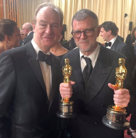 Paul Thomas Anderson holds up two Oscars statuettes while standing beside Peter Bradshaw