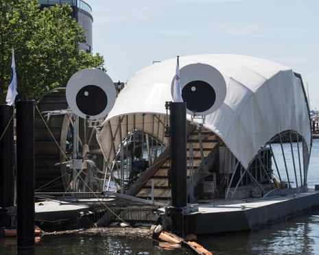 A conveyor belt lifts waste into the 'mouth' of a machine with a water wheel on one side and two 'eyes' on the top