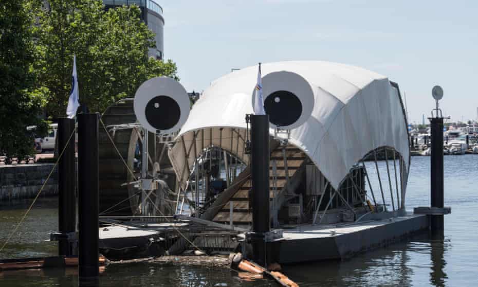 A conveyor belt lifts waste into the 'mouth' of a machine with a water wheel on one side and two 'eyes' on the top