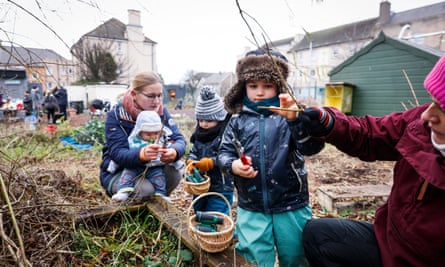 Two women and three children in the community garden. Two of the boys have plastic binoculars in wooden baskets and one of the women is helping a boy to prune a tree