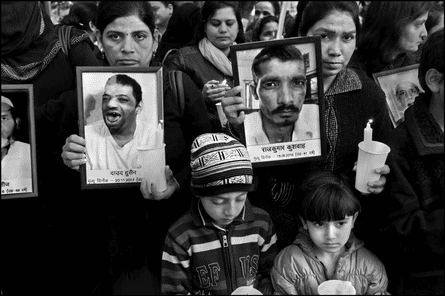 A group of women hold candles and portraits of dead relatives. Two sombre children stand at the front 