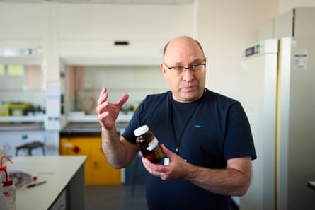 Um homem está em um laboratório segurando um frasco de vidro marrom com uma tampa branca.