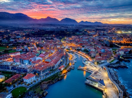 Aerial view at sunset of town by the sea with mountains behind.