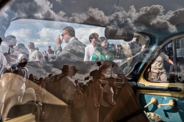 A crowd shot is reflected on a car window with a another part of the crowd pictured through the car rear window