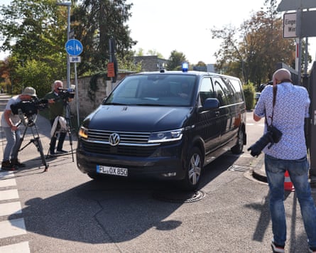 A large black car drives along a street surrounded by a handful of photographers.