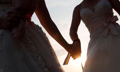A newlywed lesbian couple in wedding dresses holds hands