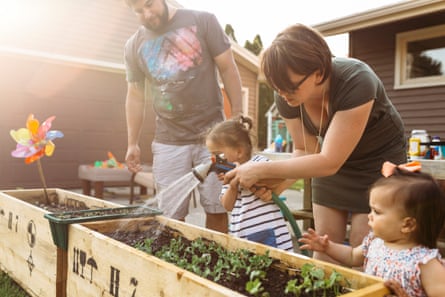 Family watering plants in a container with a hose